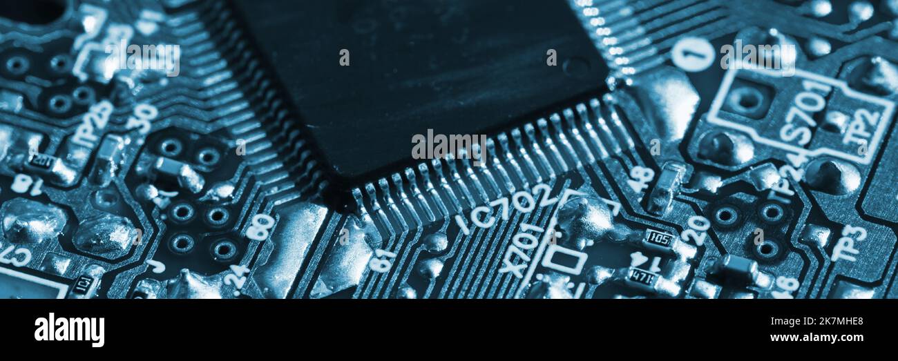 Blue toned panoramic photo of a printed circuit with microchip and capacitors, close up shot with selective focus Stock Photo