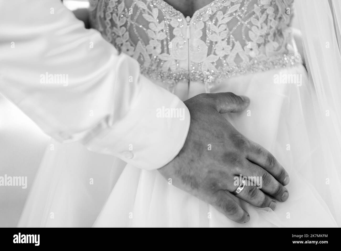 Bridal morning, bride wears dress. Groom helping fiancee to get dressed, adjusting buttons on wedding gown, rear view. close-up, crop Stock Photo