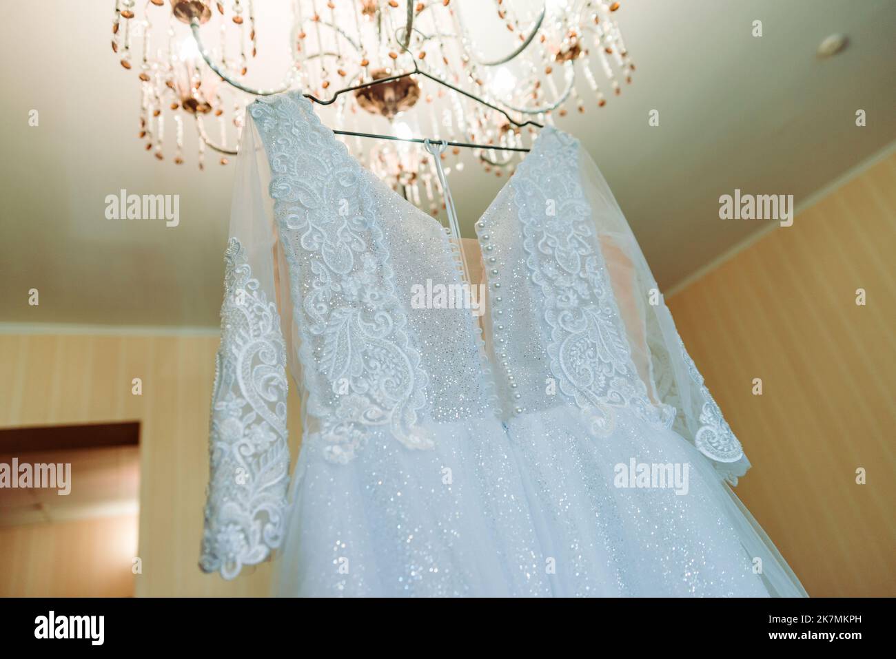 The perfect wedding dress with a full skirt on a hanger in the room of the bride with blue curtains Stock Photo