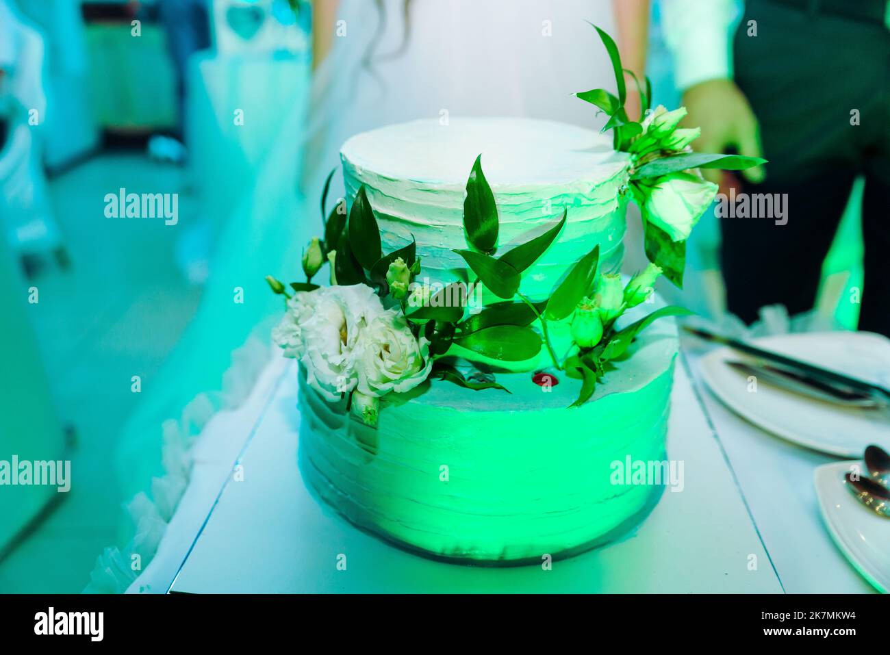 White wedding cake decorated by flowers standing on festive table with lots of snacks on side. Violet flowers on foreground. Wedding. Recetion Stock Photo