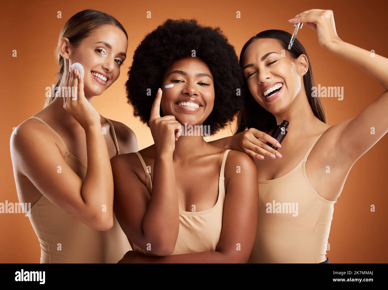 Skincare, beauty and women with product for face against an orange studio background. Portrait of a model group with oil, cream and cotton pad for Stock Photo