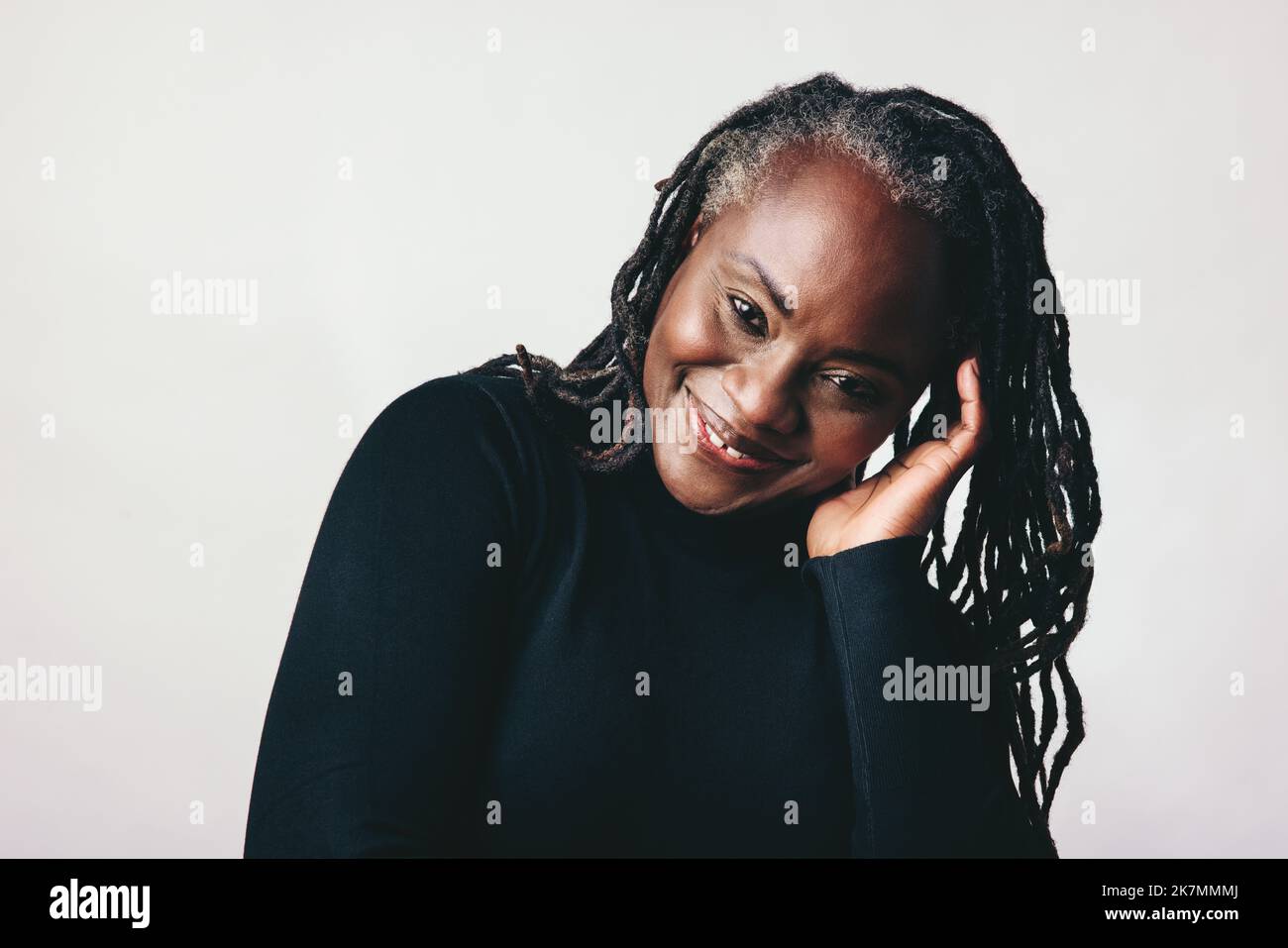 Confident mature woman smiling at the camera while touching her dreadlocks. Happy middle-aged woman embracing her natural hair with pride. Cheerful bl Stock Photo