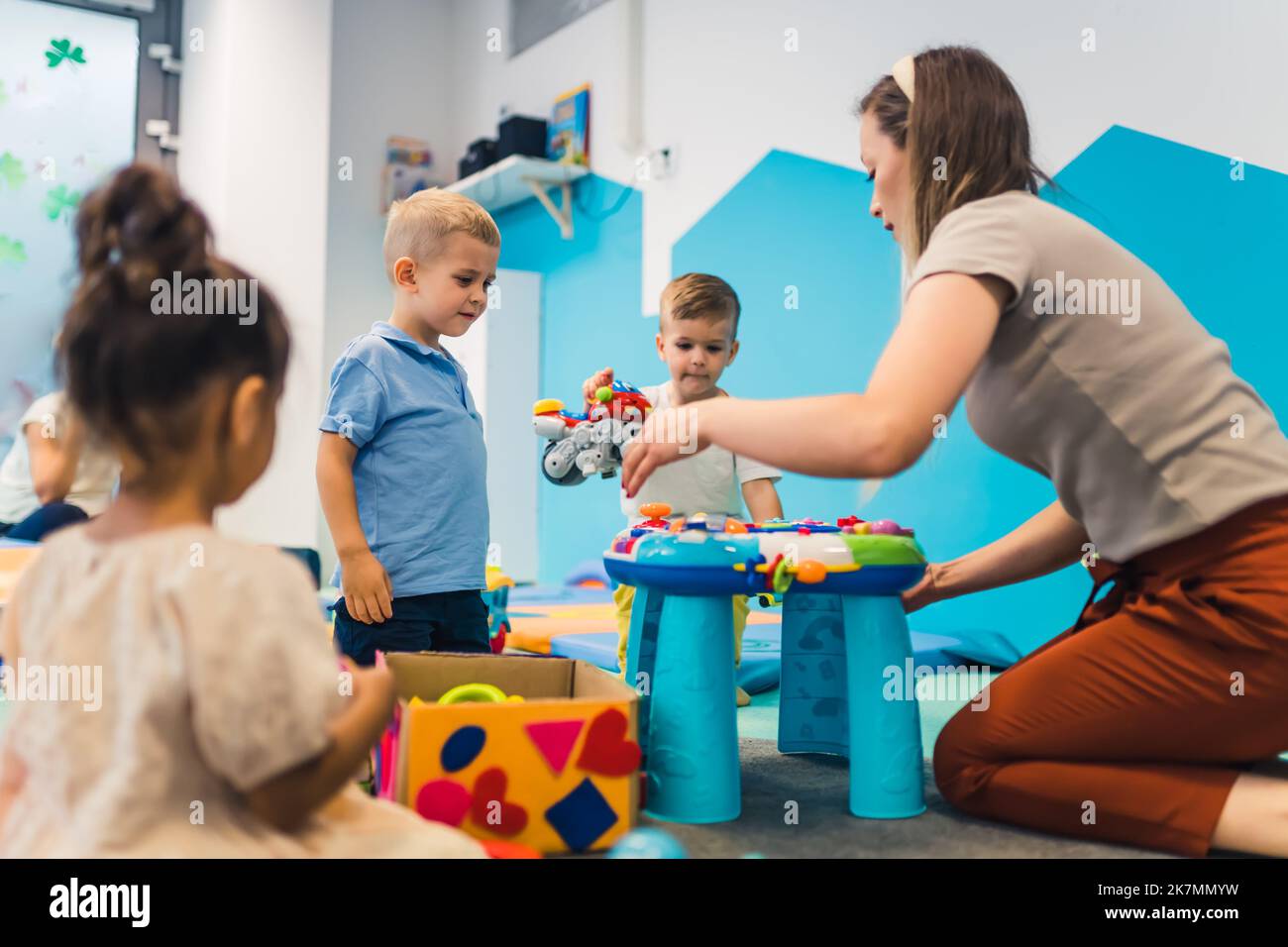 kids and a teacher sitting on the circle on the floor and playing with plastic toys, kindergarten games for preschoolers. High quality photo Stock Photo