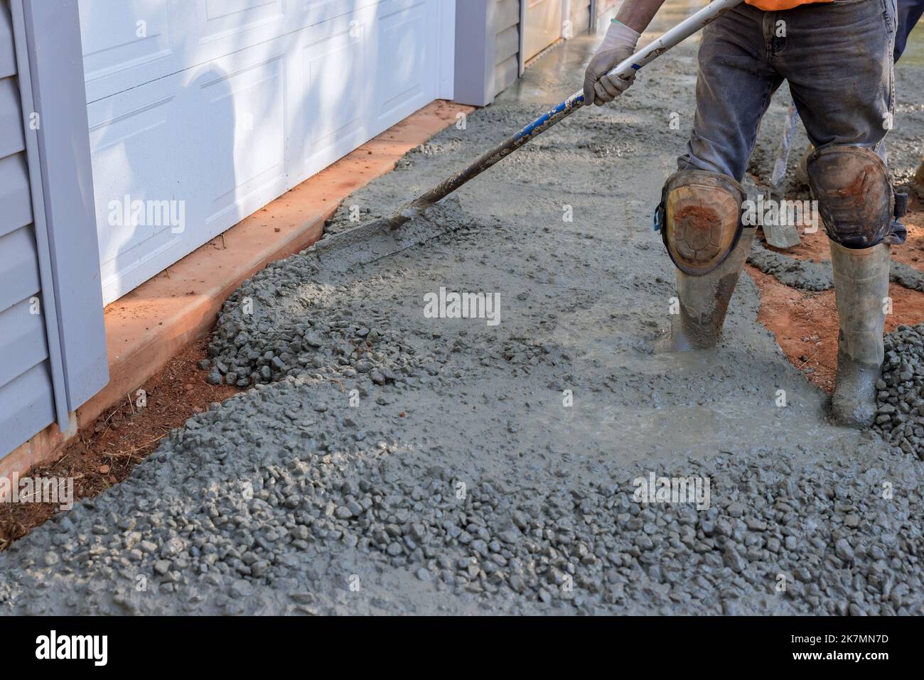 Construction contractors pouring wet concrete while paving driveway as they work on concrete