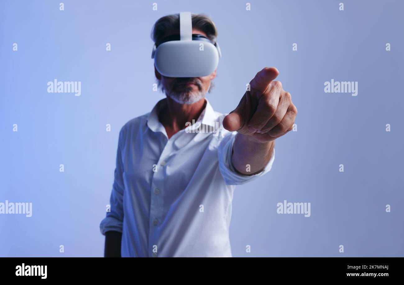 businessman interacting with virtual space while wearing virtual reality goggles. Senior businessman using his finger to press a virtual button. Matur Stock Photo