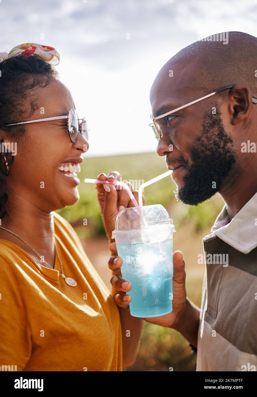 Couple, outdoor and share drink with straw together in summer with smile in sunshine. Man, black woman and happy for soda, juice or slushy on travel Stock Photo