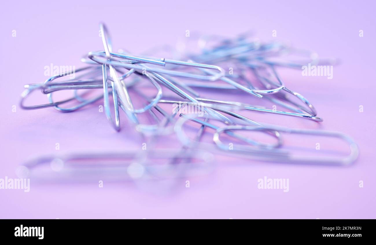 Paper clips together in pile, connected and a chain on purple background. Office supplies, organization and project management with paperclip for Stock Photo