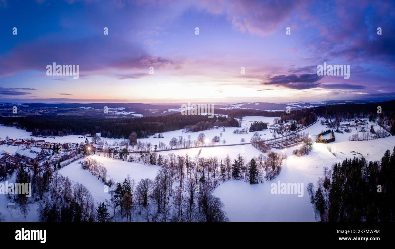 An aerial view of snow landscape with trees under purple sunset sky on ...