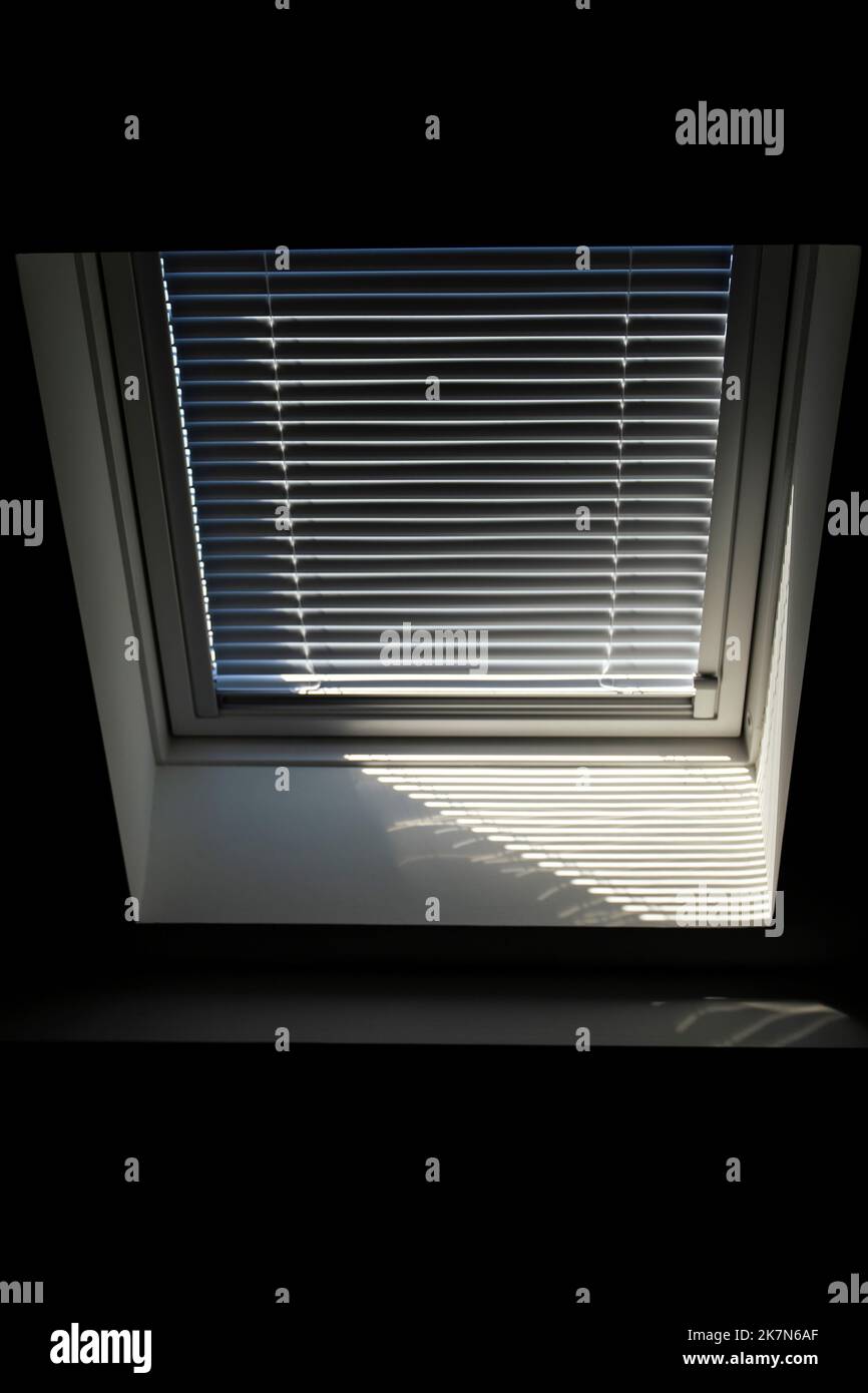 A portrait of a velux roof window with a half open jalousie in it to keep the sun and warmth out or to keep the light from entering the room in the mo Stock Photo