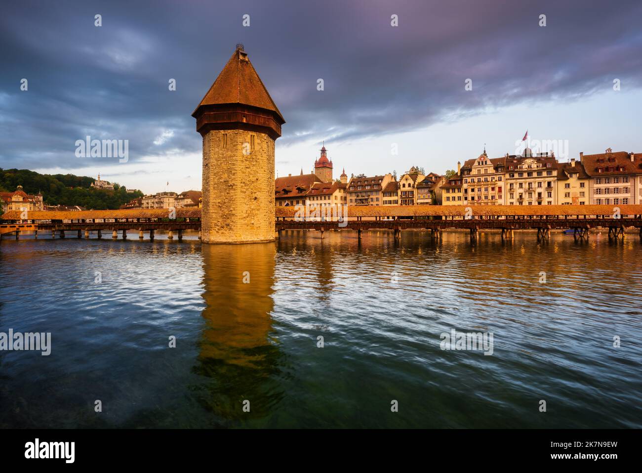 Old town of Lucerne city, Switzerland, view of the Water tower, wooden Chapel bridge and historical houses reflecting in Reuss river in dramatical sun Stock Photo
