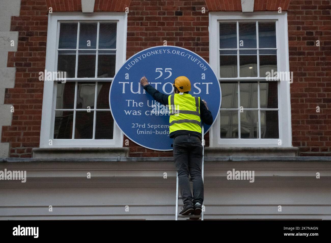 London, UK, 18 October 2022. A campaigner from Led By Donkeys fix a blue plaque to 55 Tufton Street in Westminster. The building is home to several free market groups that were instrumental in Kwarsi Kwarteng's mini budget. Credit: David Mirzoeff/Alamy Live News Stock Photo