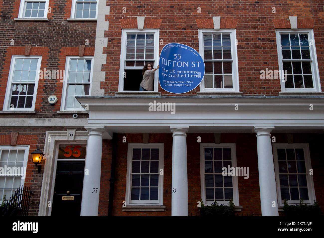 London, UK, 18 October 2022. A woman attempts to remove a blue plaque on 55 Tufton Street in Westminster, which was attached by campaigners from Led By Donkeys. The building is home to several free market groups that were instrumental in Kwarsi Kwarteng's mini budget. Credit: David Mirzoeff/Alamy Live News Stock Photo