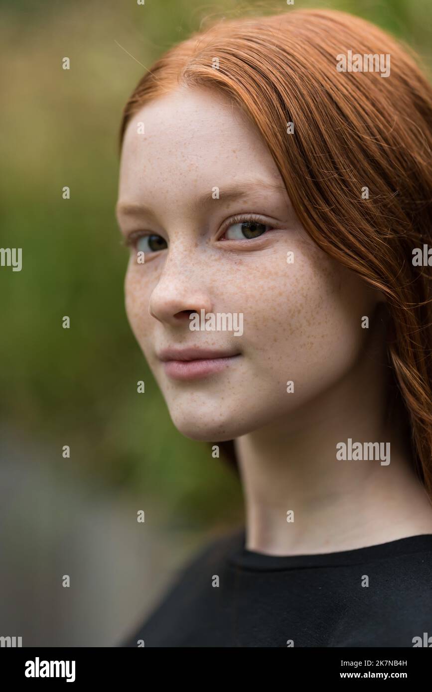 Red haired twelve year old girl with freckles posing with a nature bokeh background, Brussels, Belgium Stock Photo