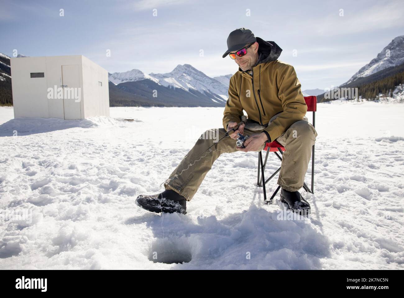 Man ice fishing on frozen alpine lake Stock Photo Alamy