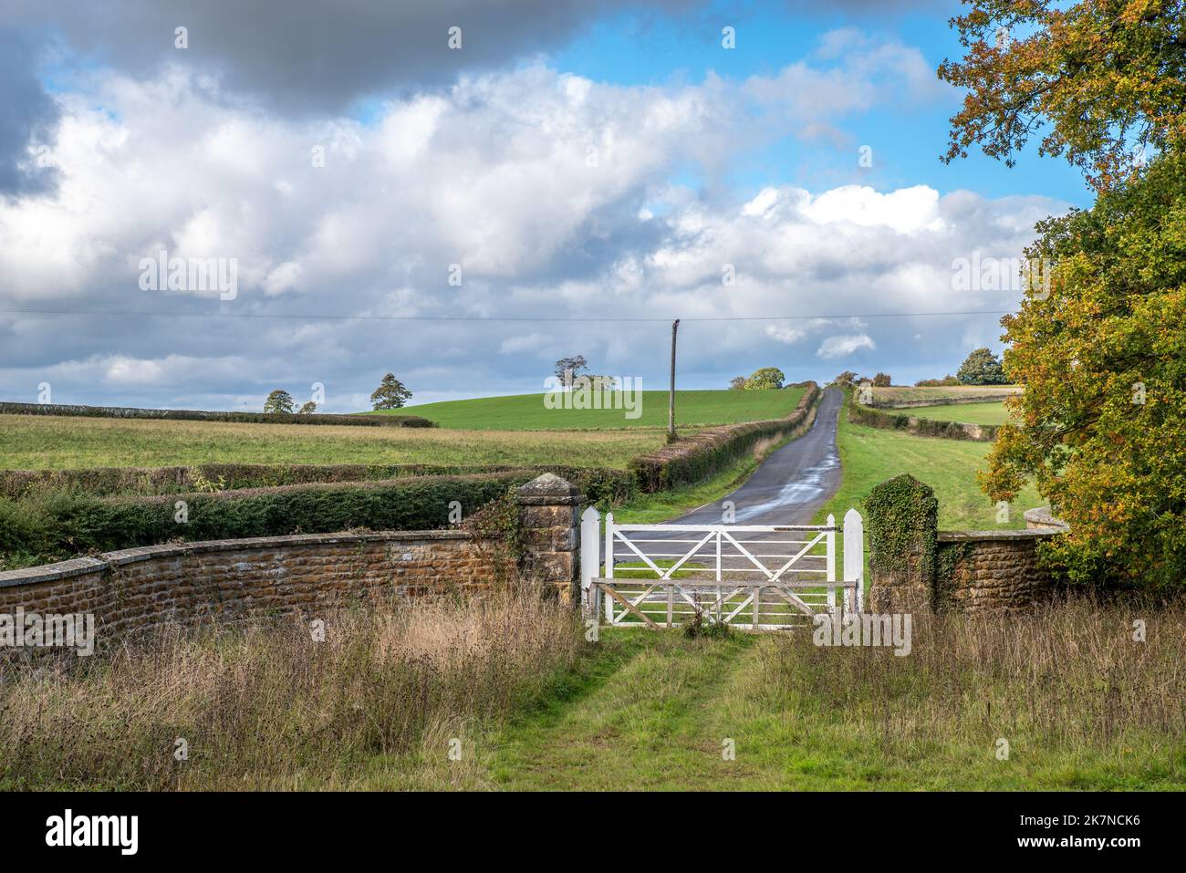 A white wooden gate leading to a country lane with a stonewall and blue