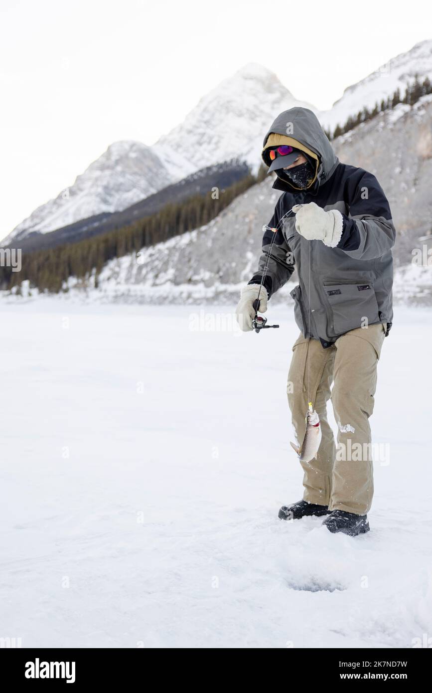 Man ice fishing on frozen alpine lake Stock Photo Alamy