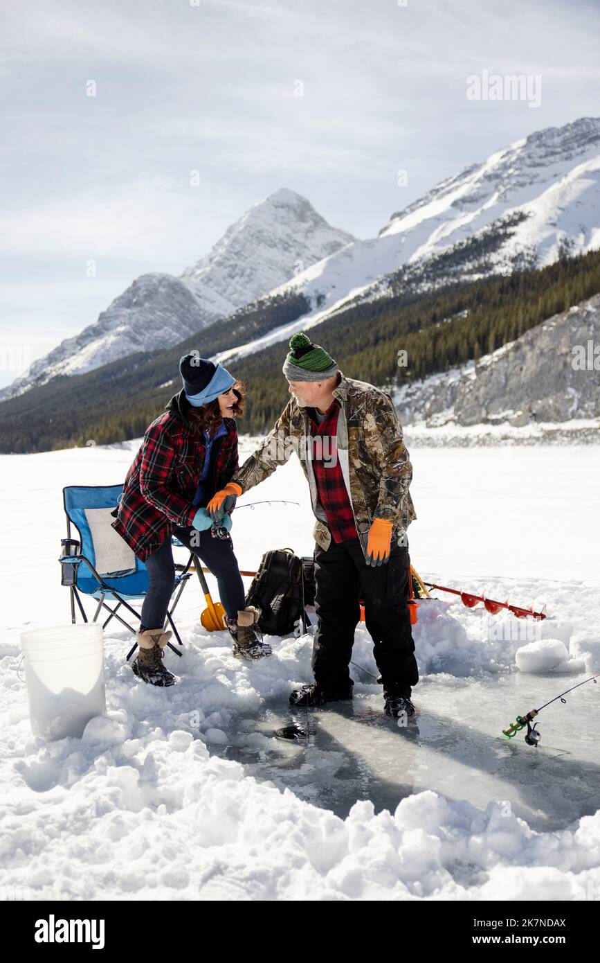 Cheerful senior couple ice fishing on frozen alpine lake Stock Photo