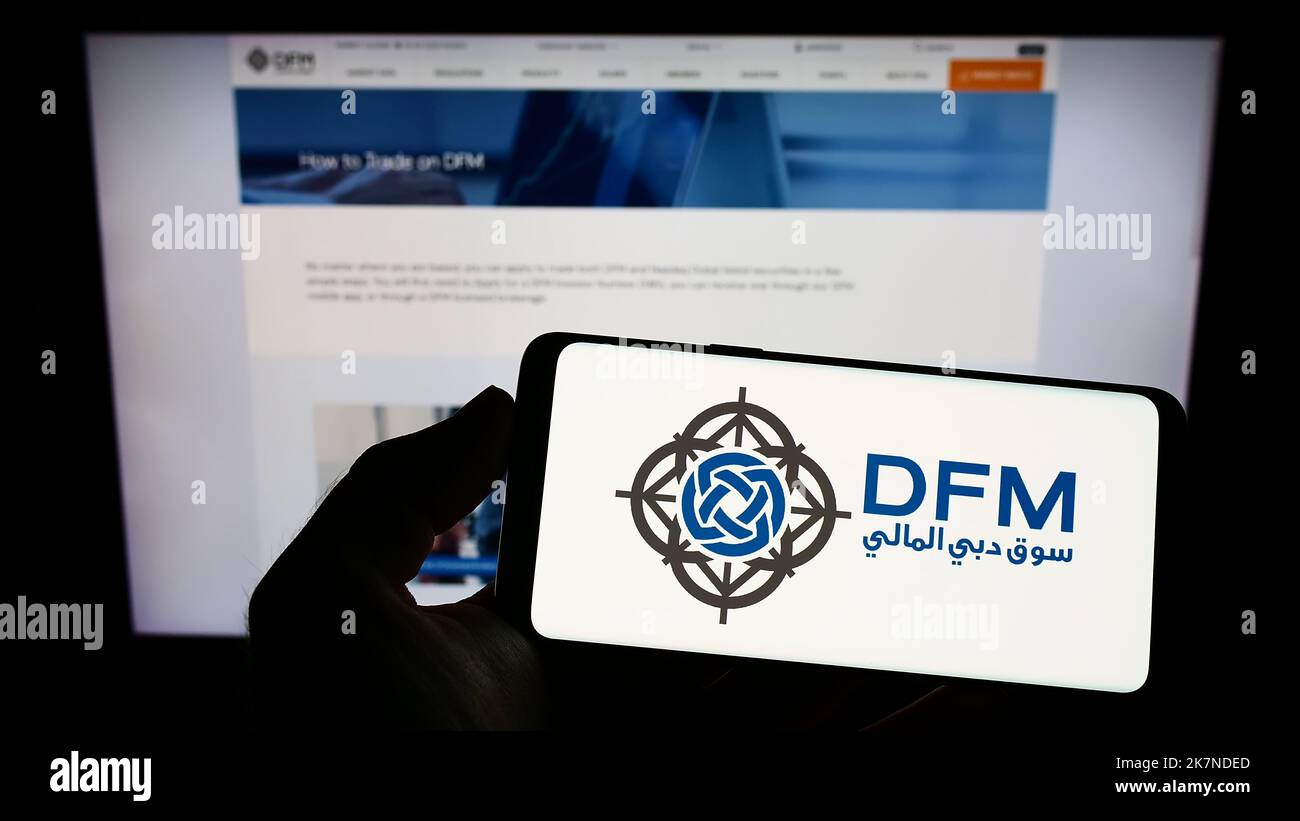 Person holding smartphone with logo of stock exchange Dubai Financial Market (DFM) on screen in front of website. Focus on phone display. Stock Photo
