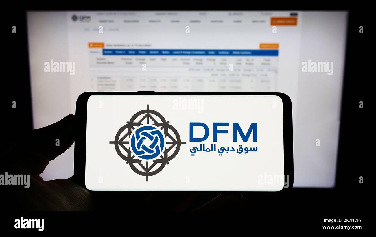 Person holding cellphone with logo of stock exchange Dubai Financial Market (DFM) on screen in front of business webpage. Focus on phone display. Stock Photo