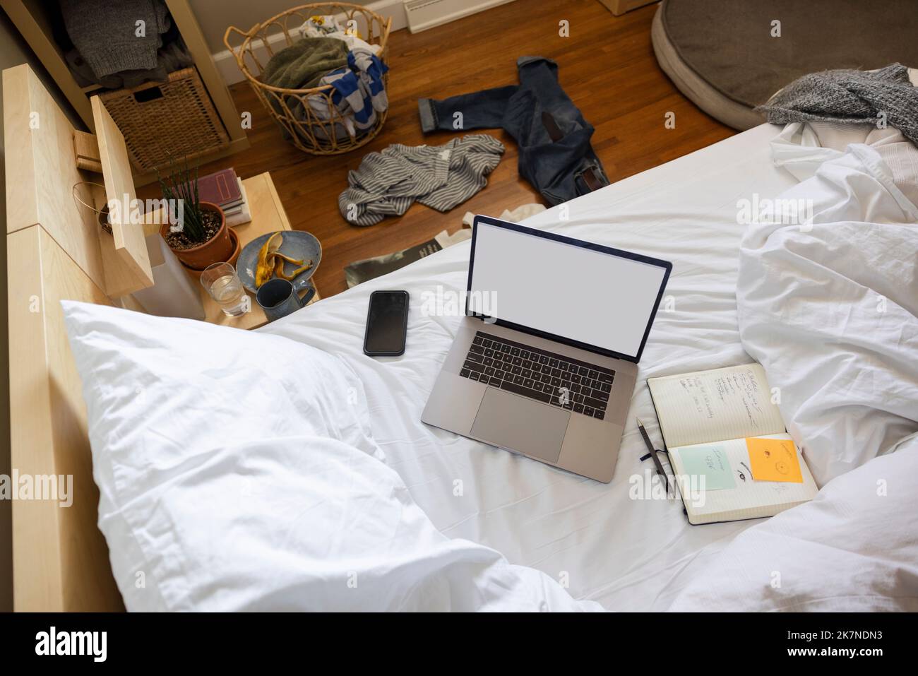 Work from home laptop and notebook on unmade bed Stock Photo