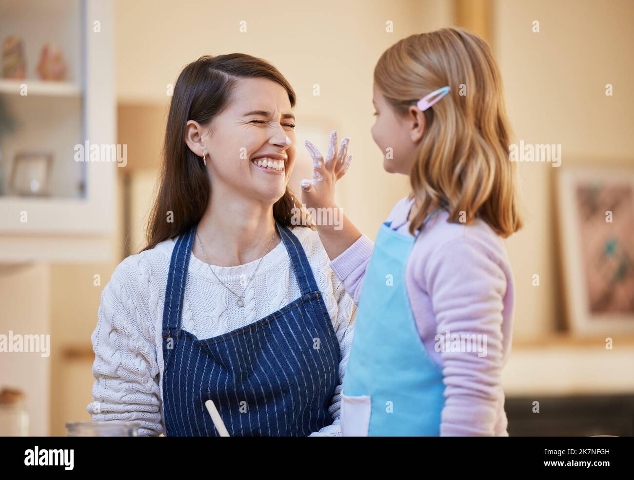 Now youre a clown. a little girl playfully putting flour on her mothers face while they bake. Stock Photo