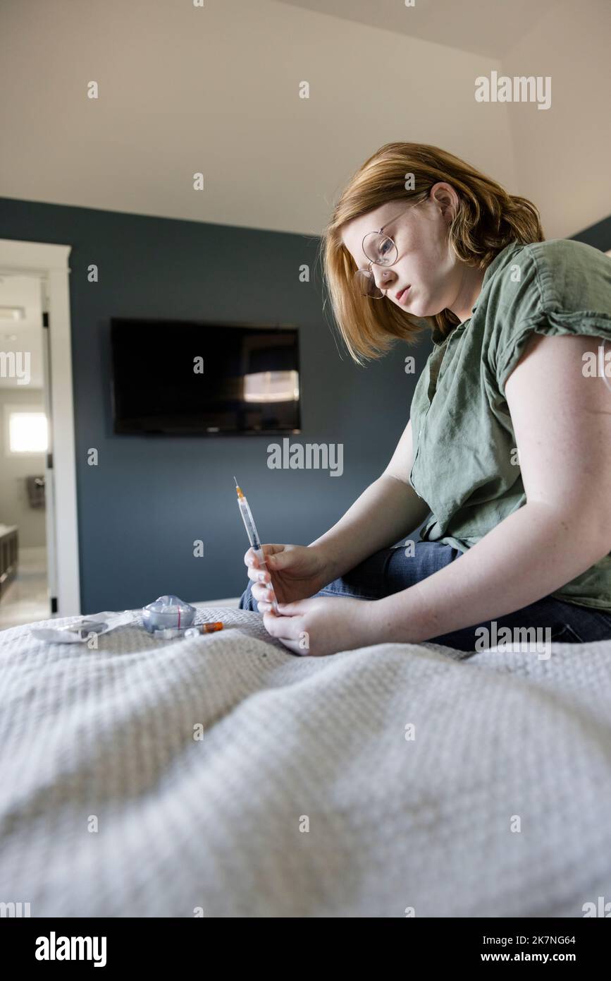 Teenage girl preparing diabetes testing equipment on bed Stock Photo