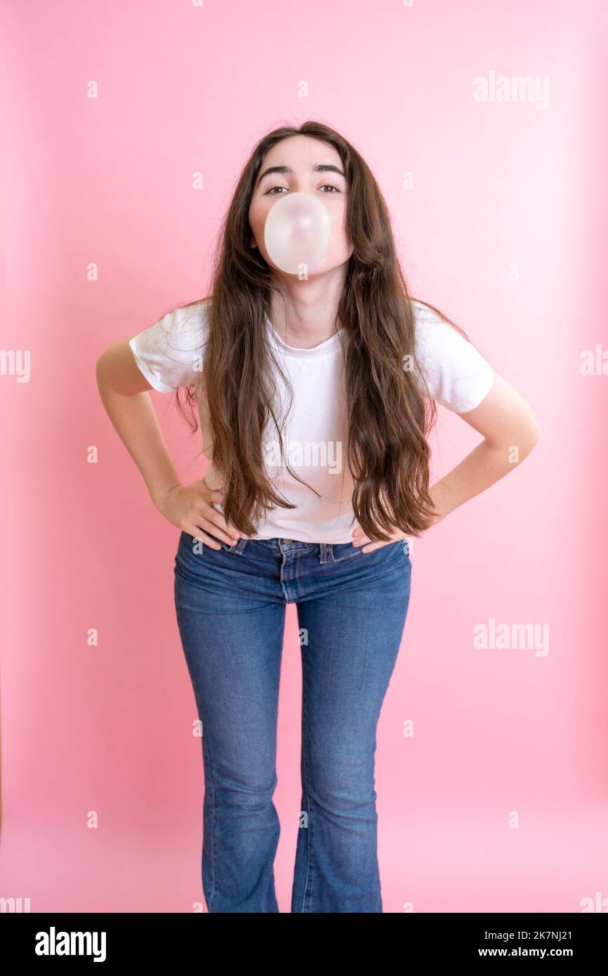 Portrait of a Young Woman Blowing Bubble Gum Bubbles Against a Pink Backdrop Stock Photo
