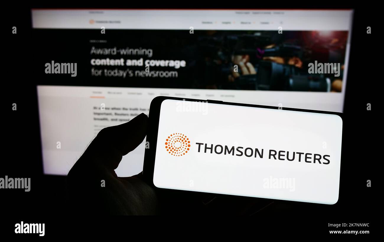 Person holding cellphone with logo of media company Thomson Reuters Corporation on screen in front of business web page. Focus on phone display. Stock Photo