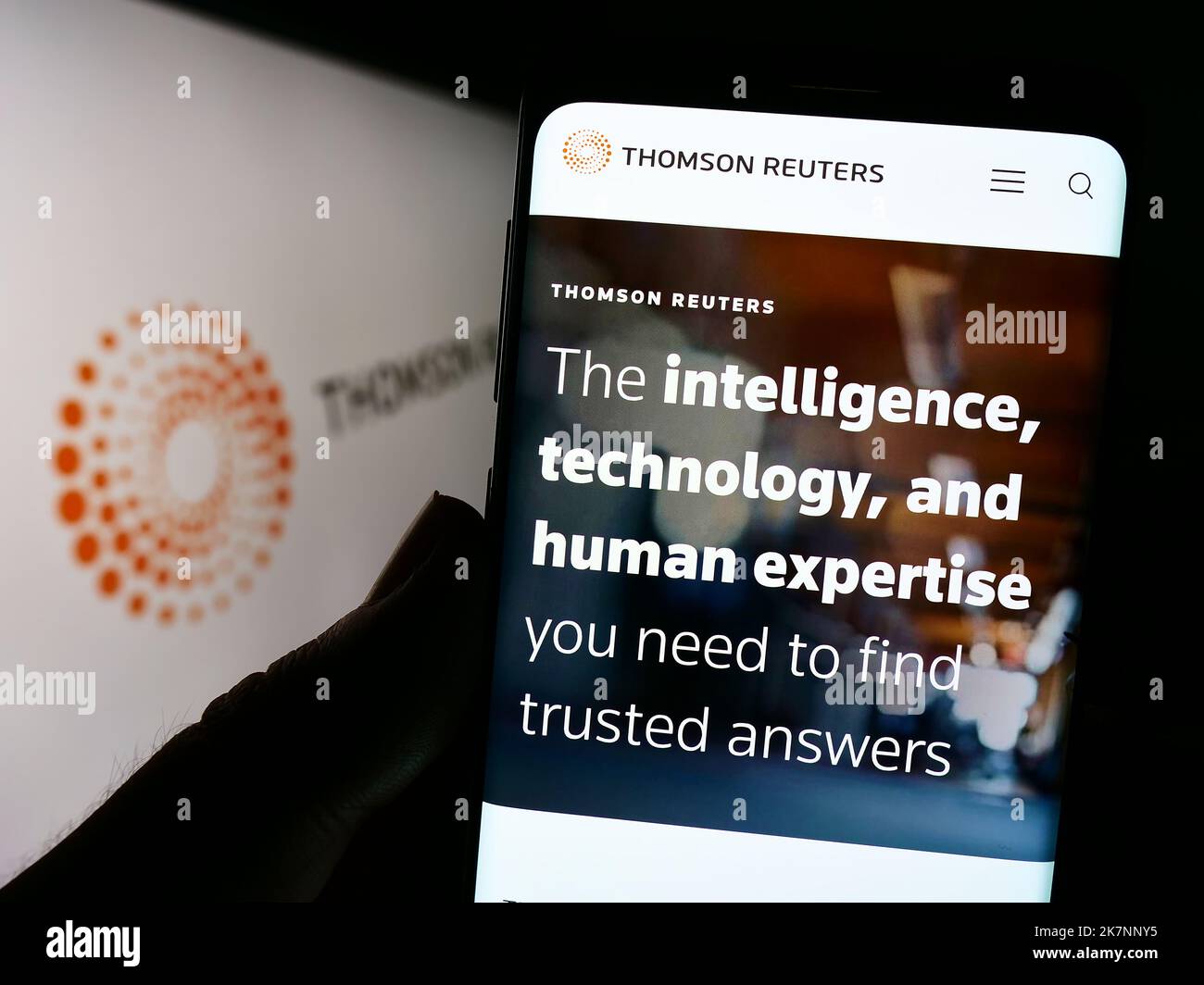 Person holding cellphone with website of media company Thomson Reuters Corporation on screen in front of logo. Focus on center of phone display. Stock Photo