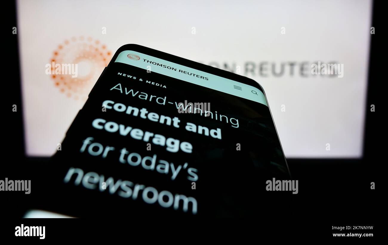 Mobile phone with webpage of media company Thomson Reuters Corporation on screen in front of business logo. Focus on top-left of phone display. Stock Photo