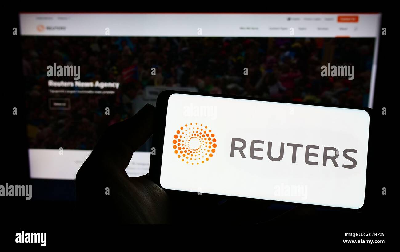 Person holding smartphone with logo of news agency Reuters on screen in front of website. Focus on phone display. Stock Photo
