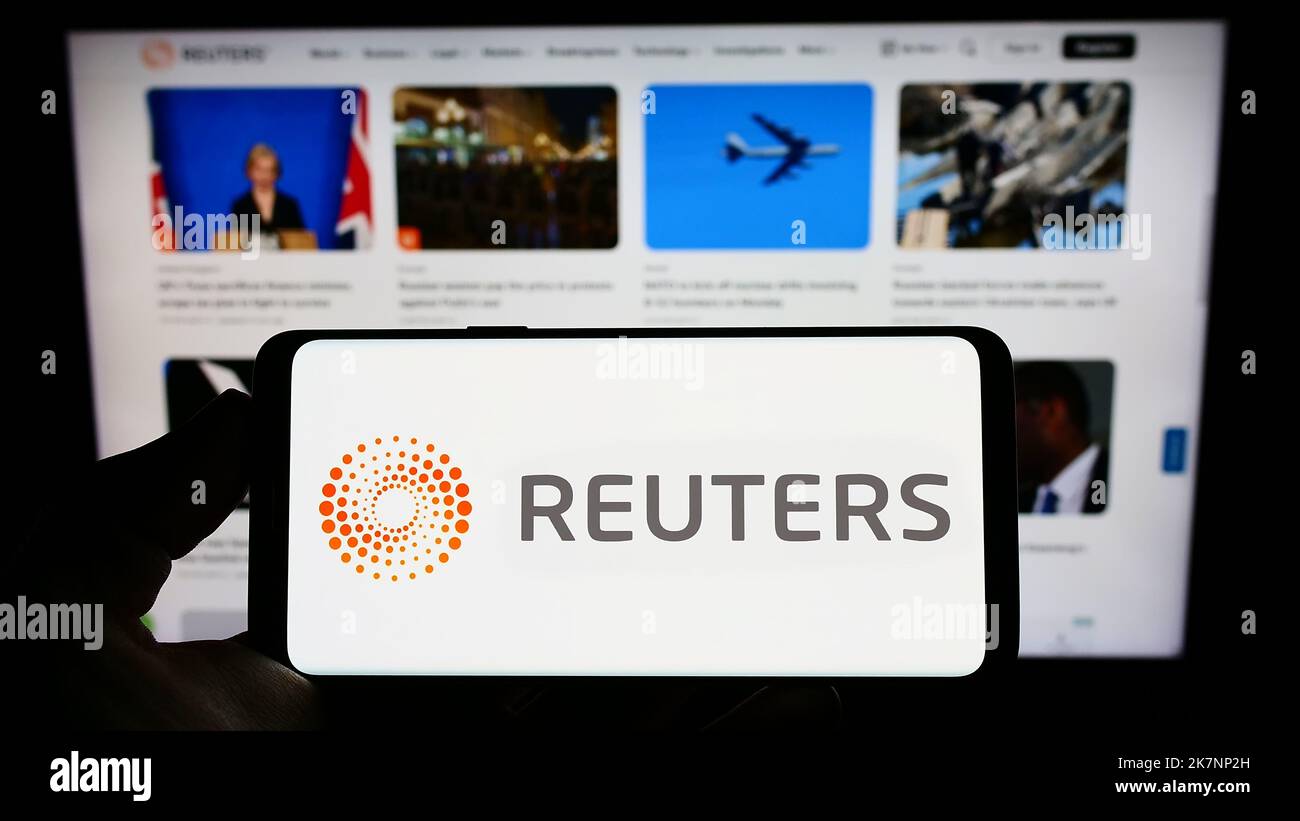 Person holding cellphone with logo of news agency Reuters on screen in front of business webpage. Focus on phone display. Stock Photo