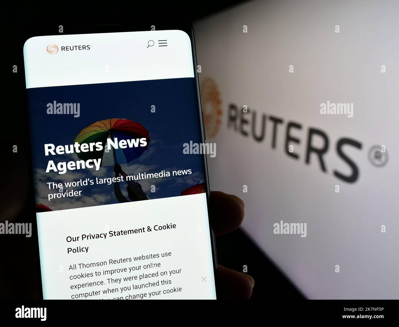 Person holding cellphone with webpage of news agency Reuters on screen in front of business logo. Focus on center of phone display. Stock Photo