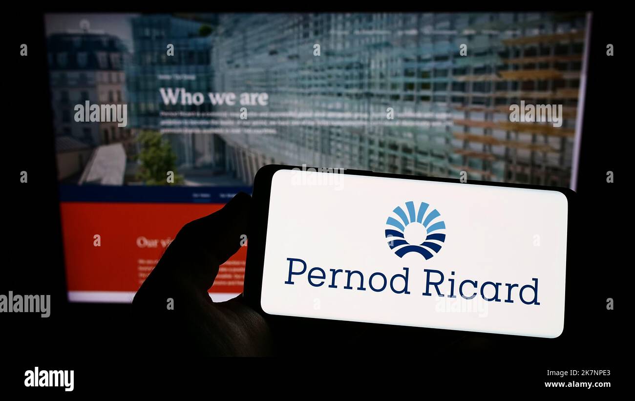 Person holding smartphone with logo of French beverage company Pernod Ricard S.A. on screen in front of website. Focus on phone display. Stock Photo