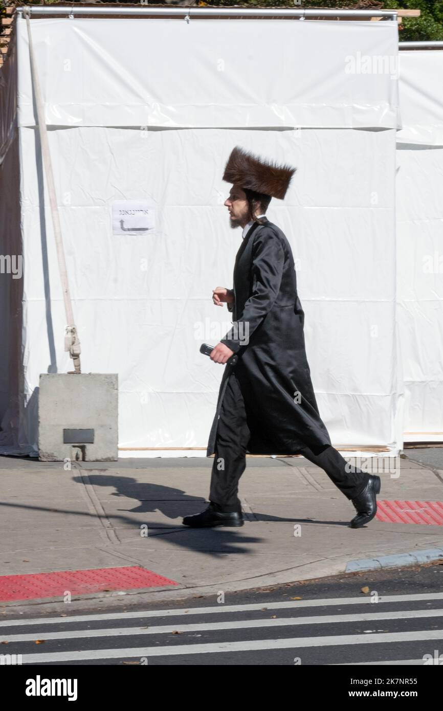 A Hasidic Jewish man walks past a Sukkah wearing a shtreimel fur hat. In Brooklyn, New York City. Stock Photo