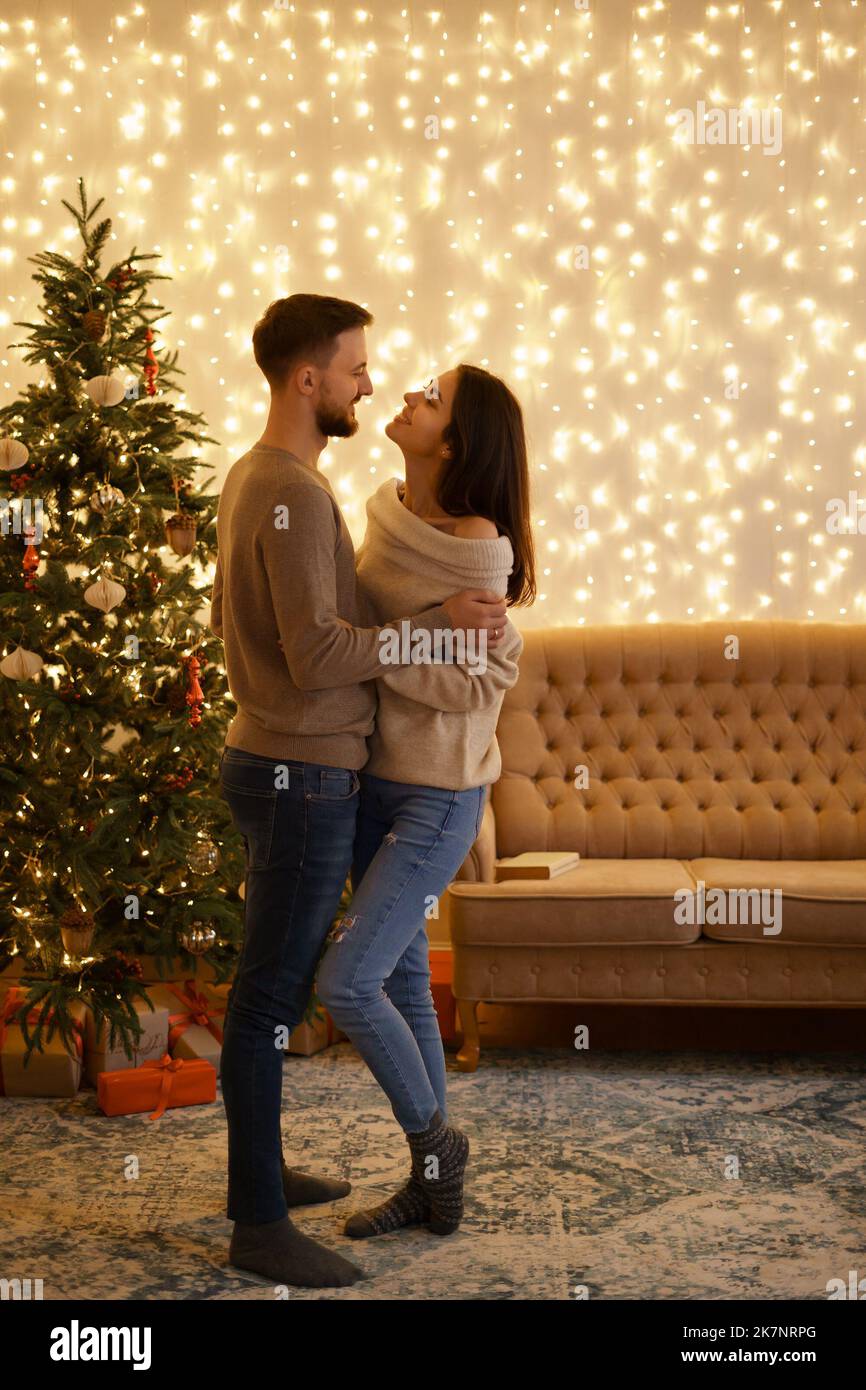 Two cheerful lovely sweet tender beautiful adorable cute romantic married spouses husband and wife enfolding near fir tree in house Stock Photo