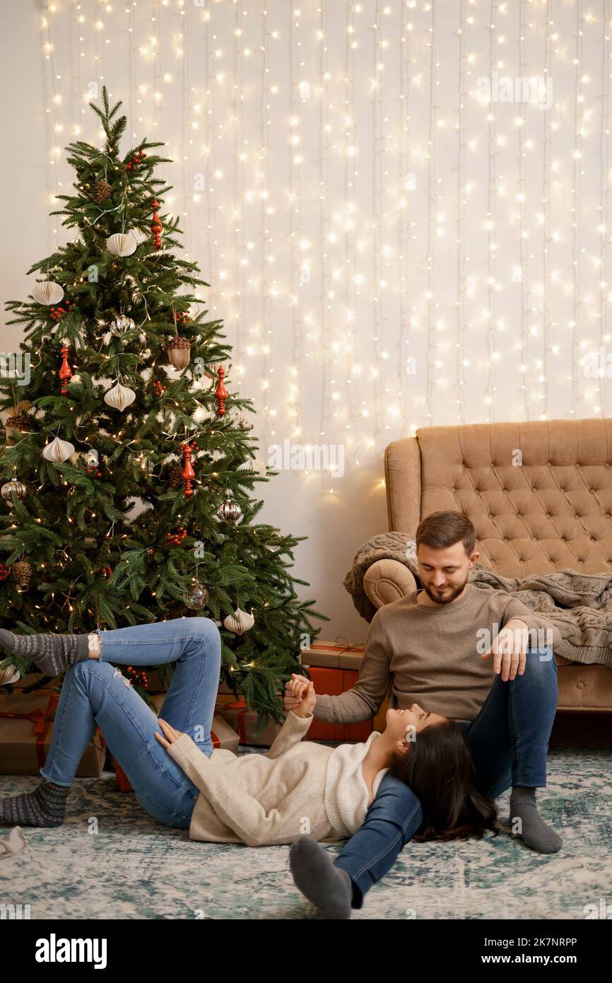 Two cheerful lovely sweet tender beautiful adorable cute romantic married spouses husband and wife enfolding near fir tree in house Stock Photo