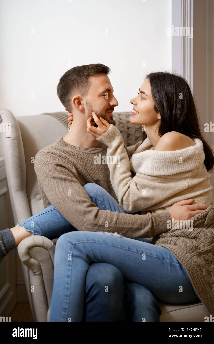 Romantic couple at home. An Attractive young woman and handsome man are enjoying spending time together while siting coddling on the armchair Stock Photo