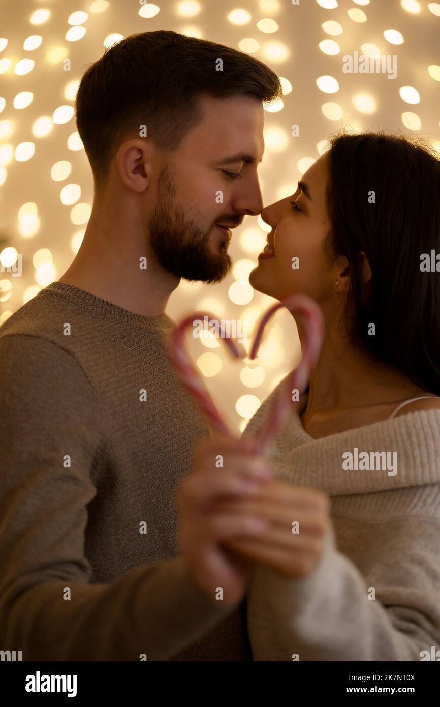 Holiday loving family portrait kissing and showing candy heart with bokeh lights in background. Focus on couple Stock Photo