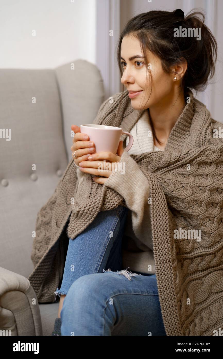 Smiling lady in smart trendy wear is sitting on armchair with a cup of tea. Smiling, sitting in relaxing atmosphere indoors at home, nice design. Stock Photo
