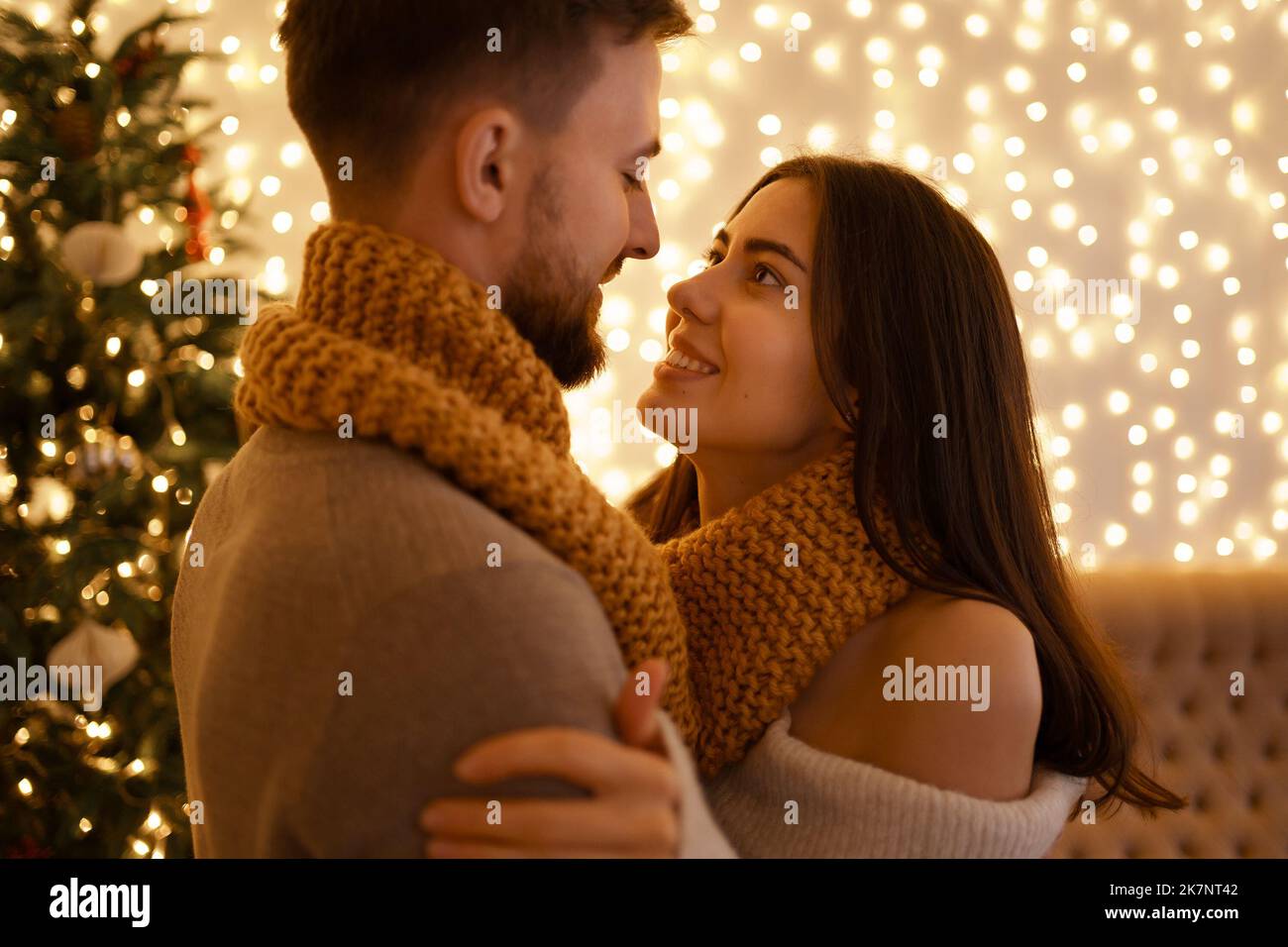 Two cheerful lovely sweet tender beautiful adorable cute romantic married spouses husband and wife enfolding in one snood fot two near fir tree in house Stock Photo