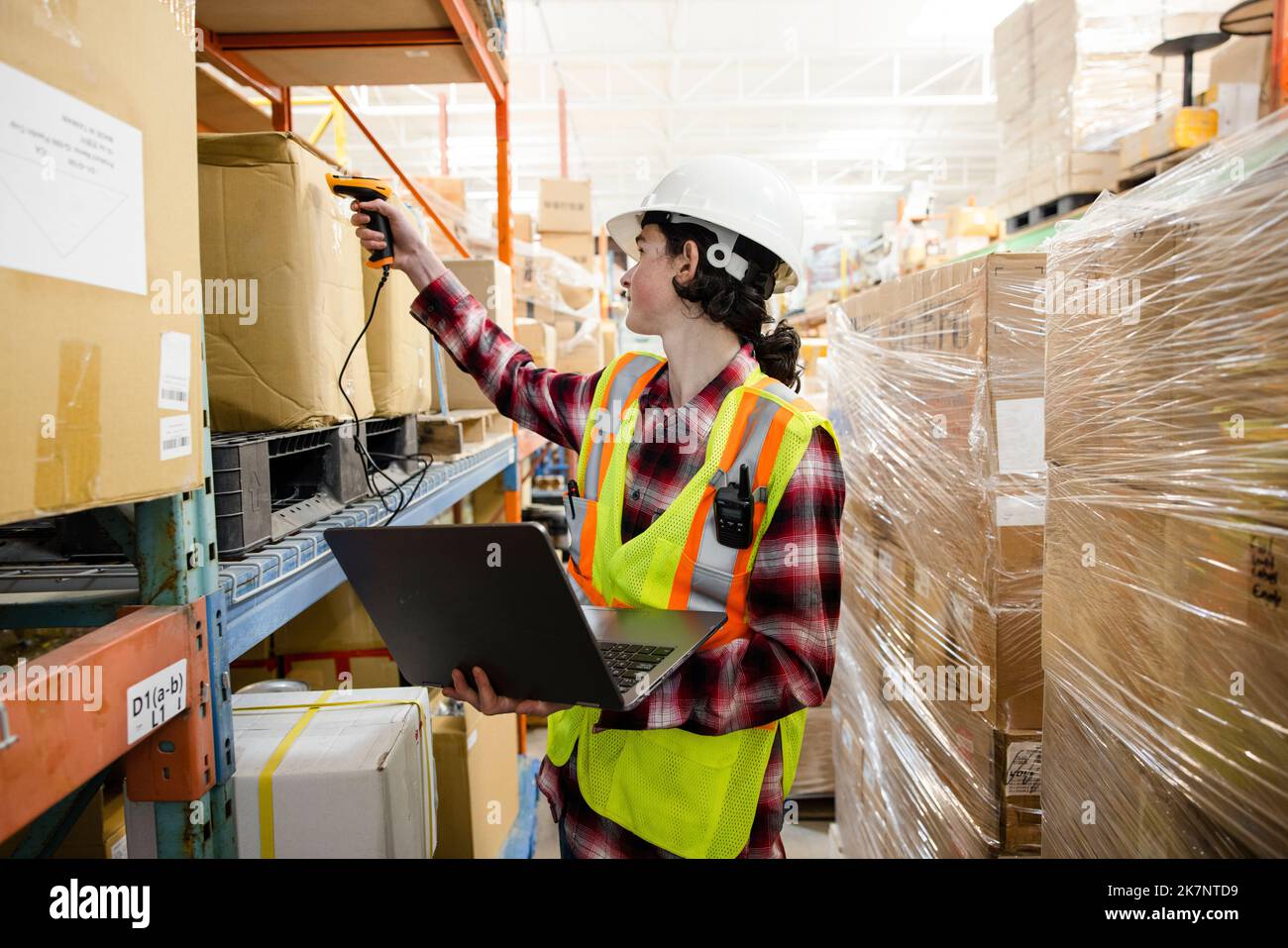 Male warehouse worker with laptop scanning boxes on shelf Stock Photo