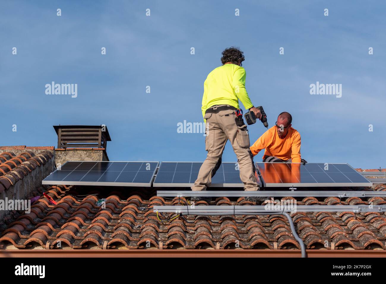 People Installing Roof with two people installing solar panels and a blue sky with white ...