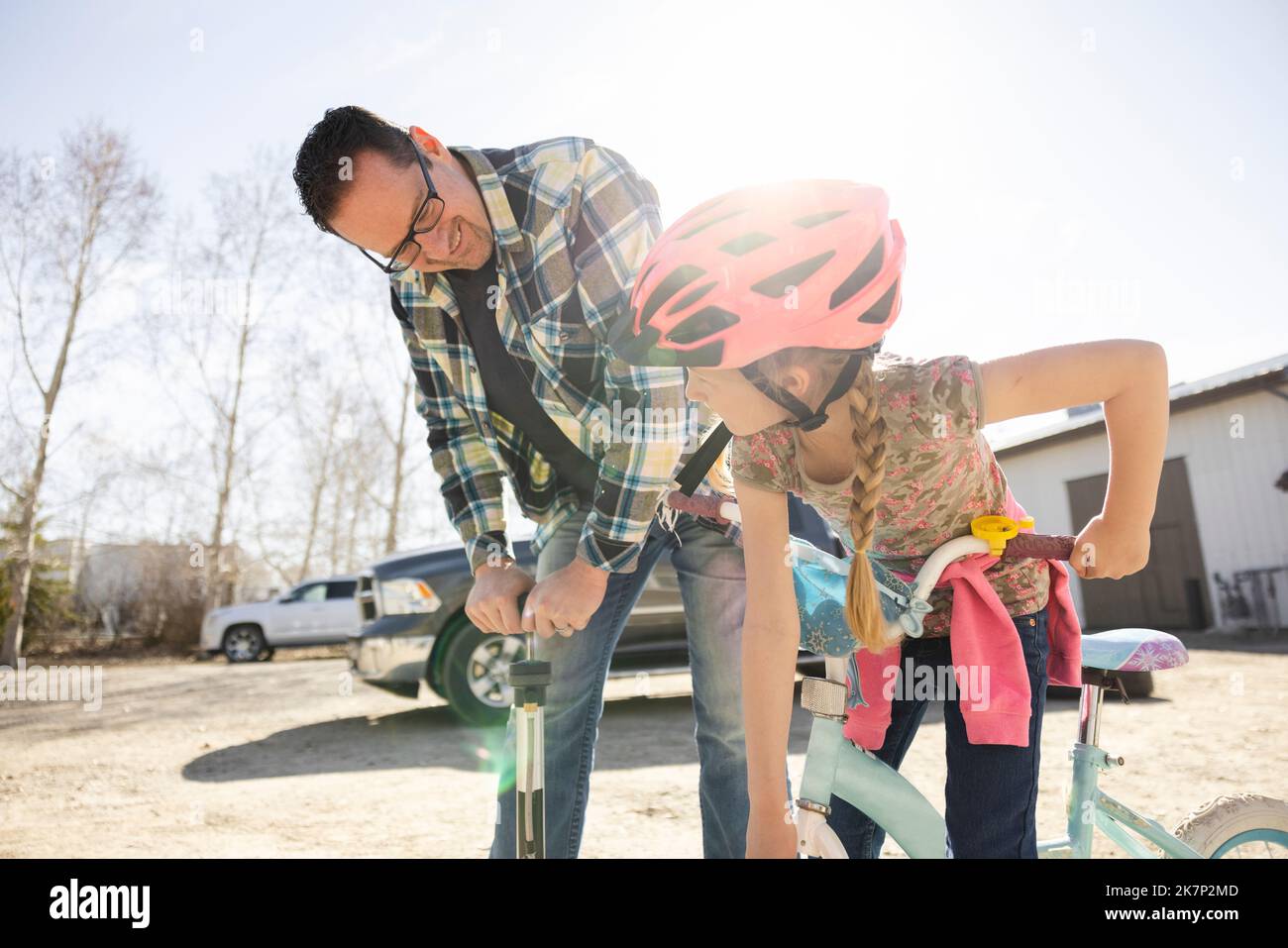 Helpful father pumping bicycle wheel for daughter in yard Stock Photo