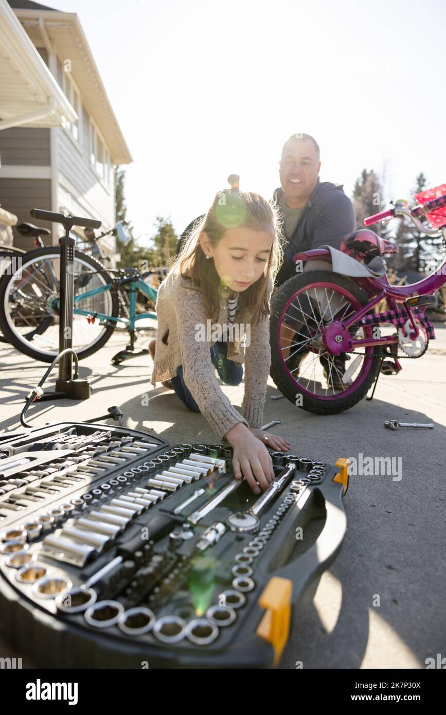 Daughter helping father fix bicycle in driveway Stock Photo
