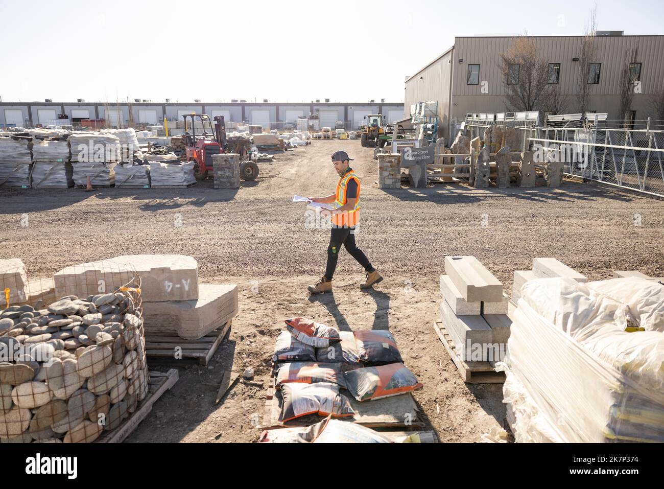 Worker walking past building materials in industrial yard Stock Photo