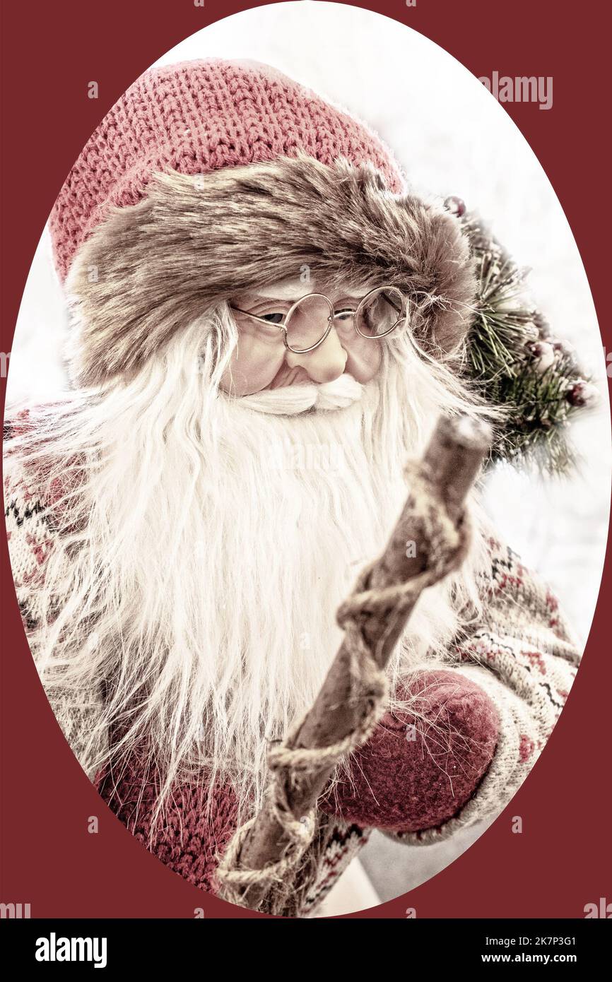 Old fashioned woodland Christmas Santa with knit fir trimmed hat and spectacles holding walking stick - Vintage filter with oval frame and dark red ba Stock Photo