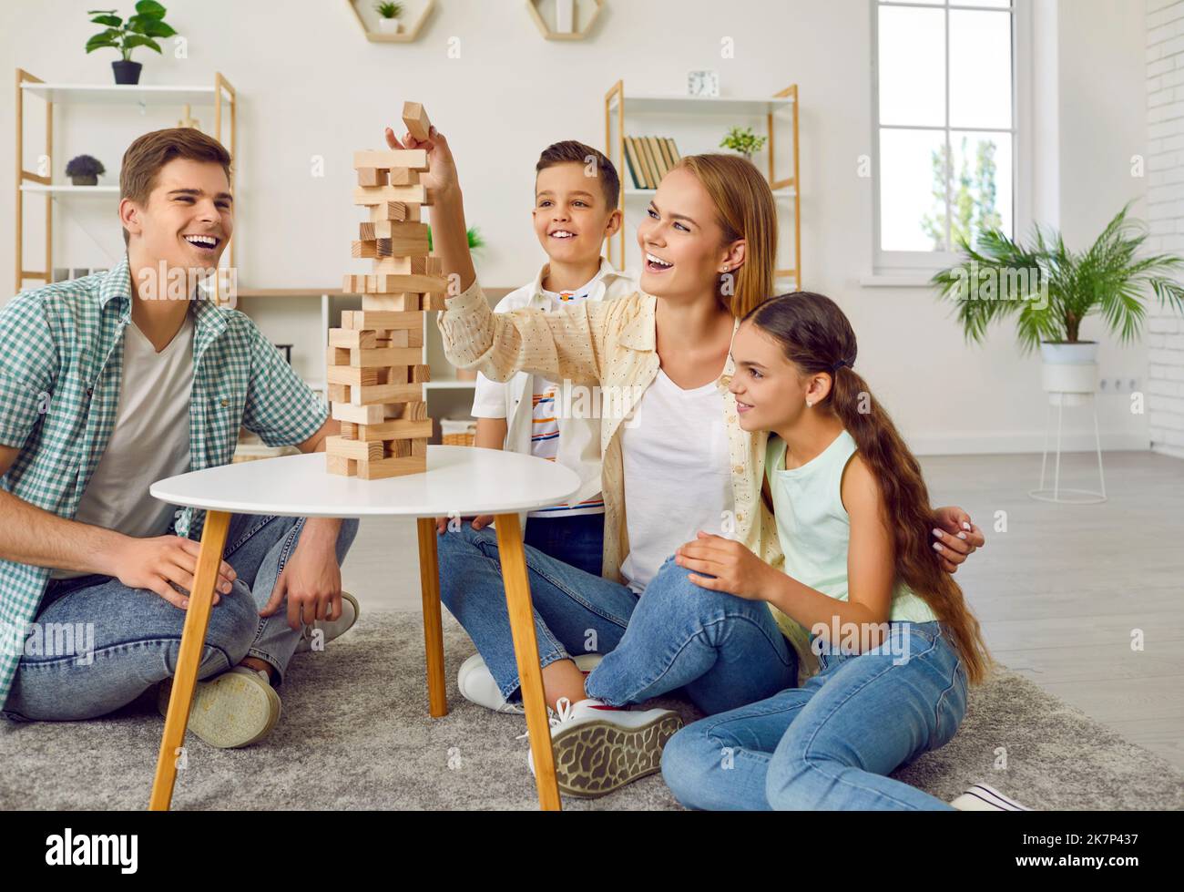 Happy family with two children are playing tumbling tower sitting on floor at home. Stock Photo