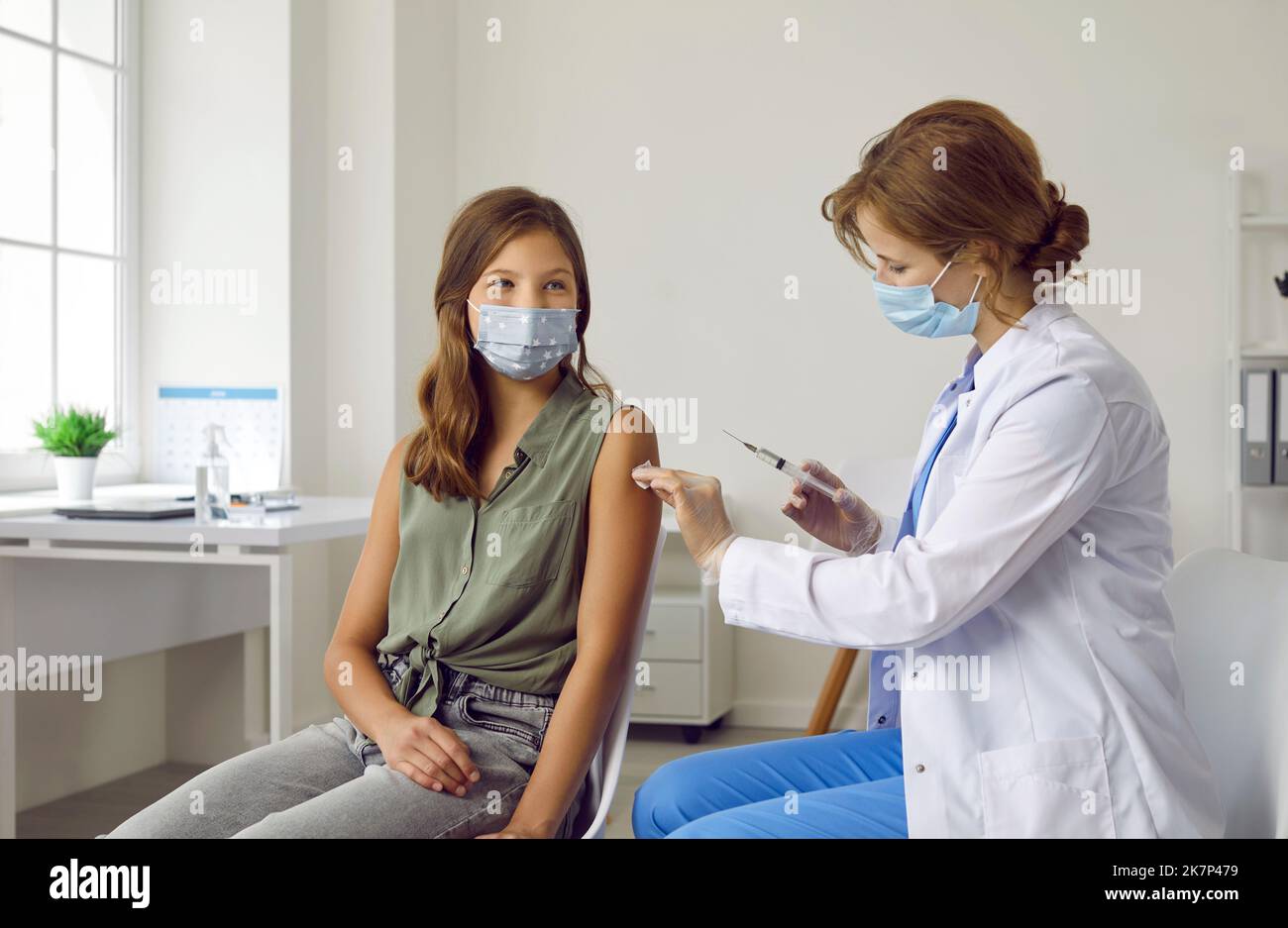 Smiling brave teenage girl wearing mask receives dose of coronavirus vaccine at vaccination center. Stock Photo