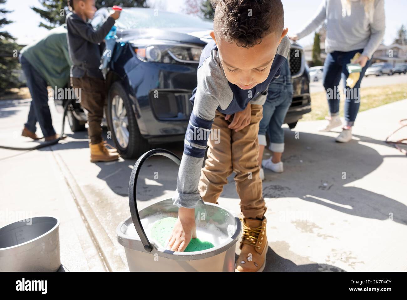 Boy dipping sponge into bucket of soapy foam in driveway Stock Photo